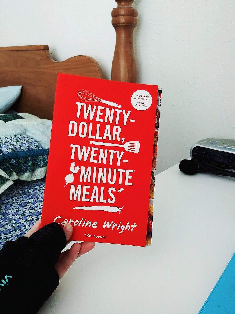 Hand, in a brace, holding "Twenty-Dollar Twenty-Minute Meals" cookbook by Caroline Wright
