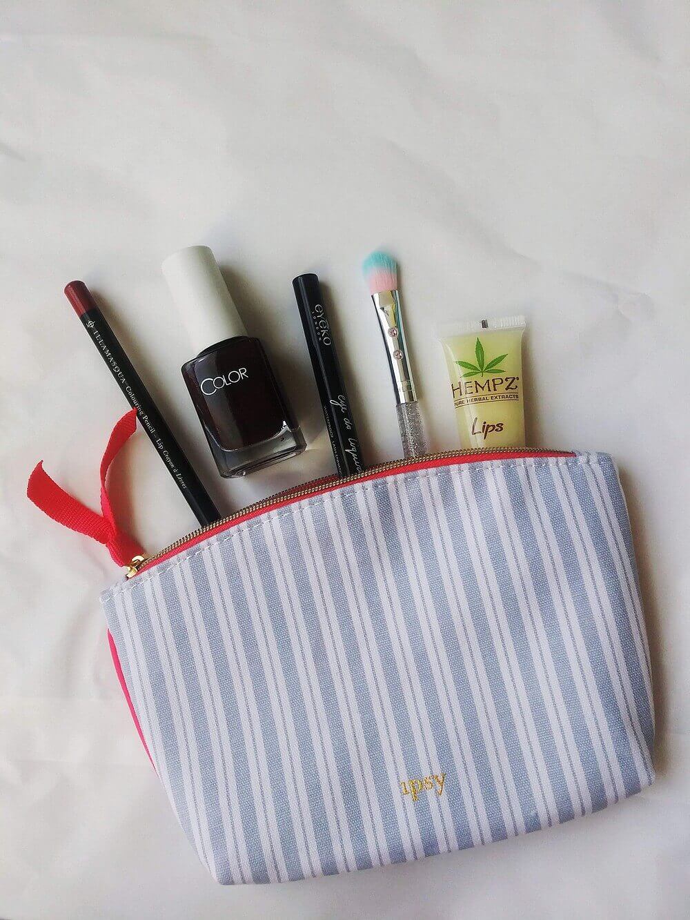 Contents (described in headers below) partially inside a striped cosmetic bag lined with hot pink