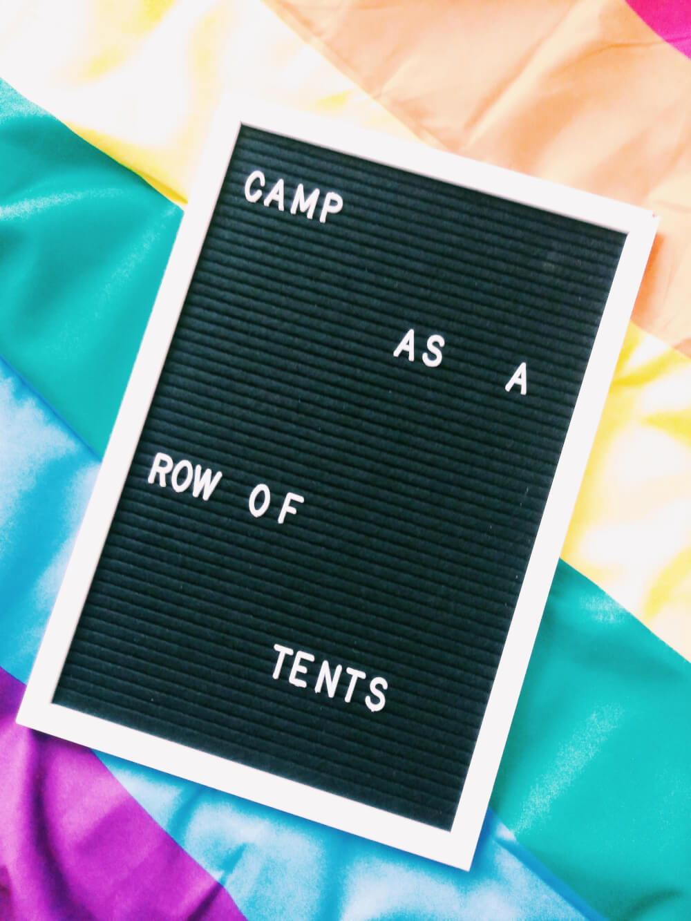 Letter board that says "Camp as a row of tents" atop a gay Pride flag