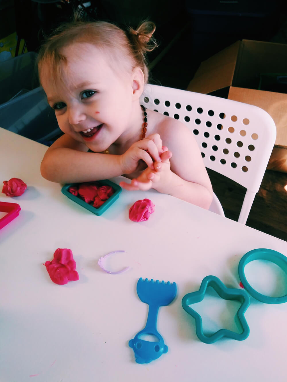 Caucasion toddler looking at photographer and giggling, while holding Playdough in hands