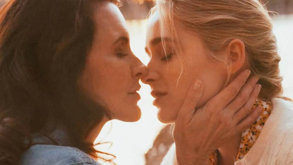 Brunette woman holding blonde woman close for a kiss
