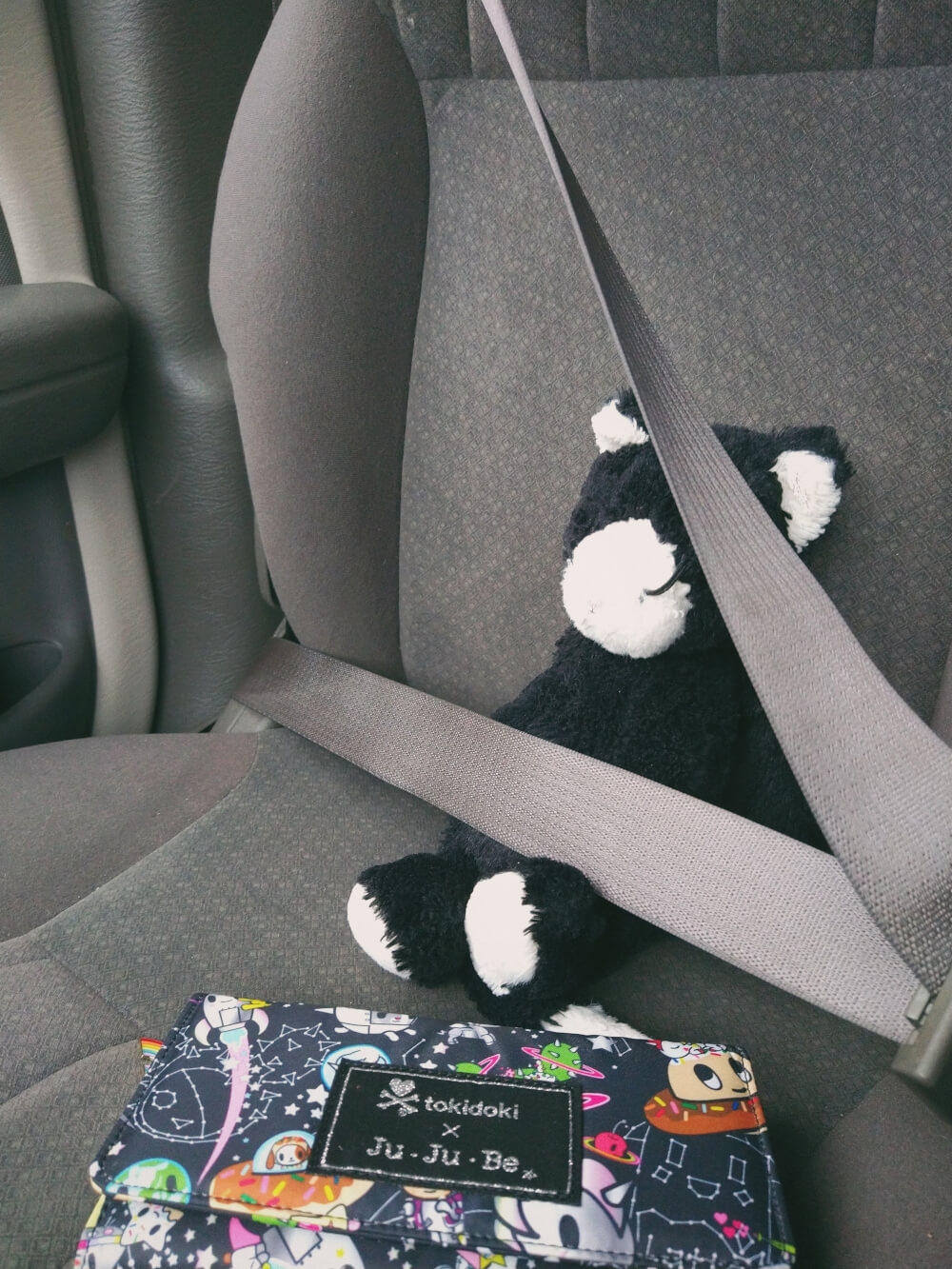 Stuffed cat buckled into front car seat, colorful wallet