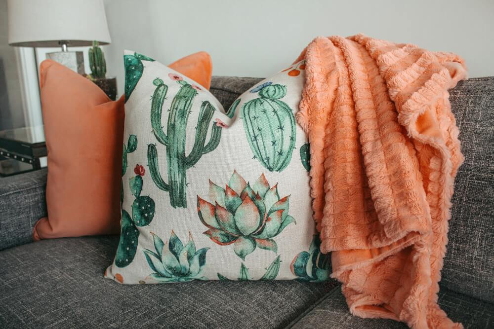 Coral pillow and succulent pillow on grey couch, with coral throw